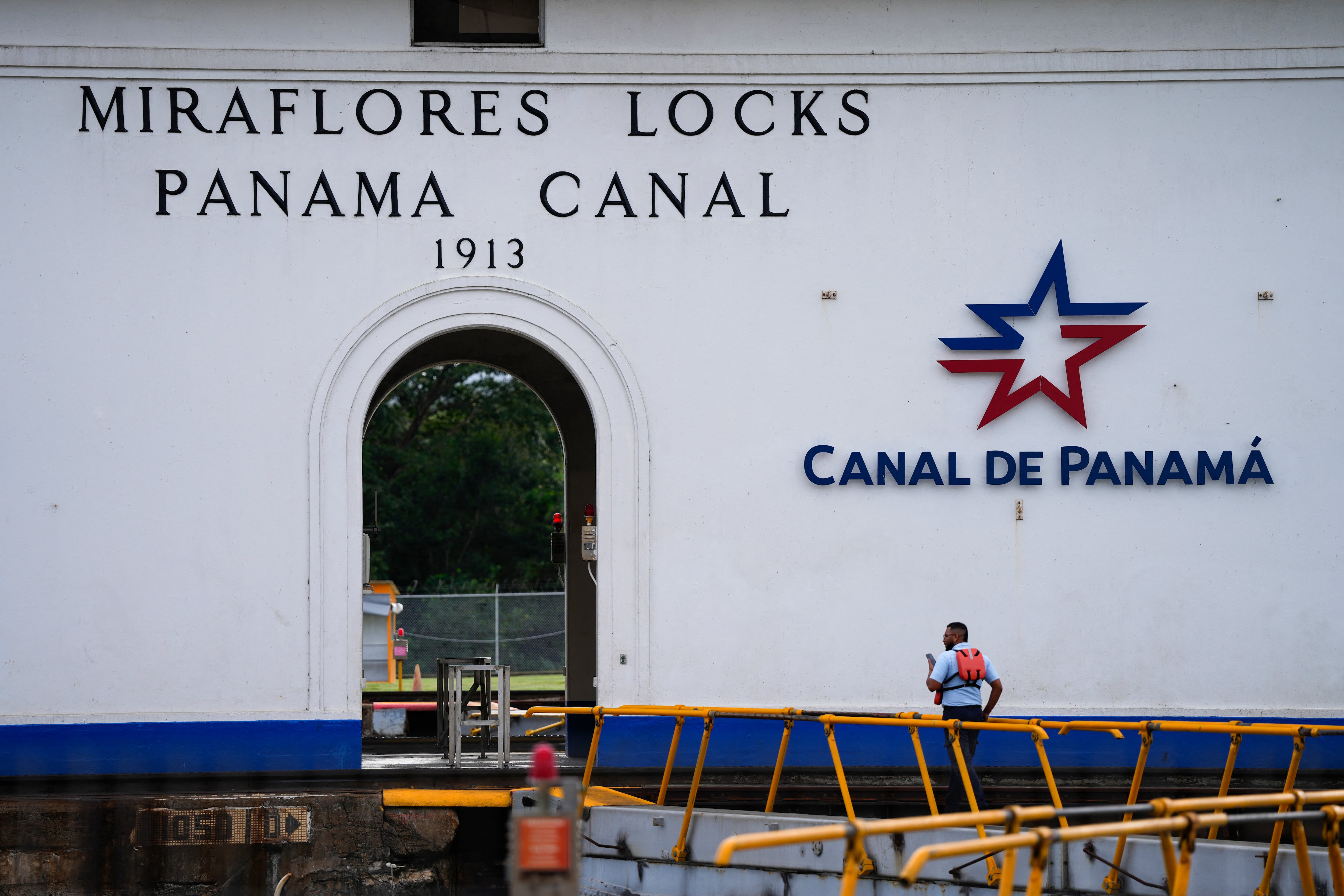 Fotografía de las esclusas de Miraflores en el Canal de Panamá, con un trabajador caminando sobre la pasarela de seguridad. En la pared se observan inscripciones que identifican la infraestructura y el logotipo de la Autoridad del Canal de Panamá.