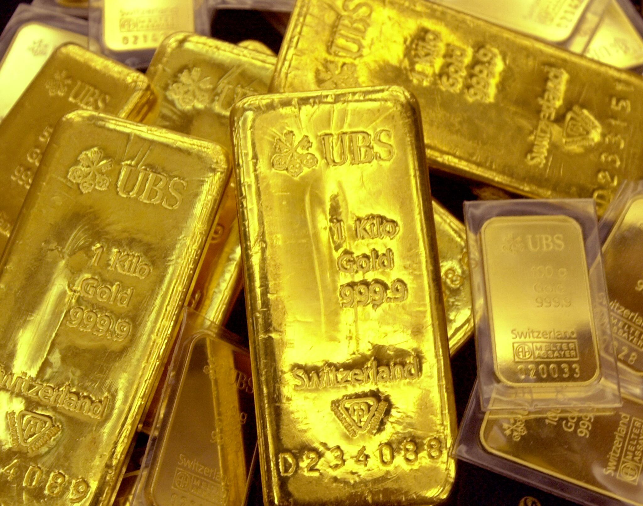 Varios lingotes de oro con inscripciones de UBS y su pureza en quilates, destacando el papel del metal precioso como inversión segura en tiempos de incertidumbre económica.