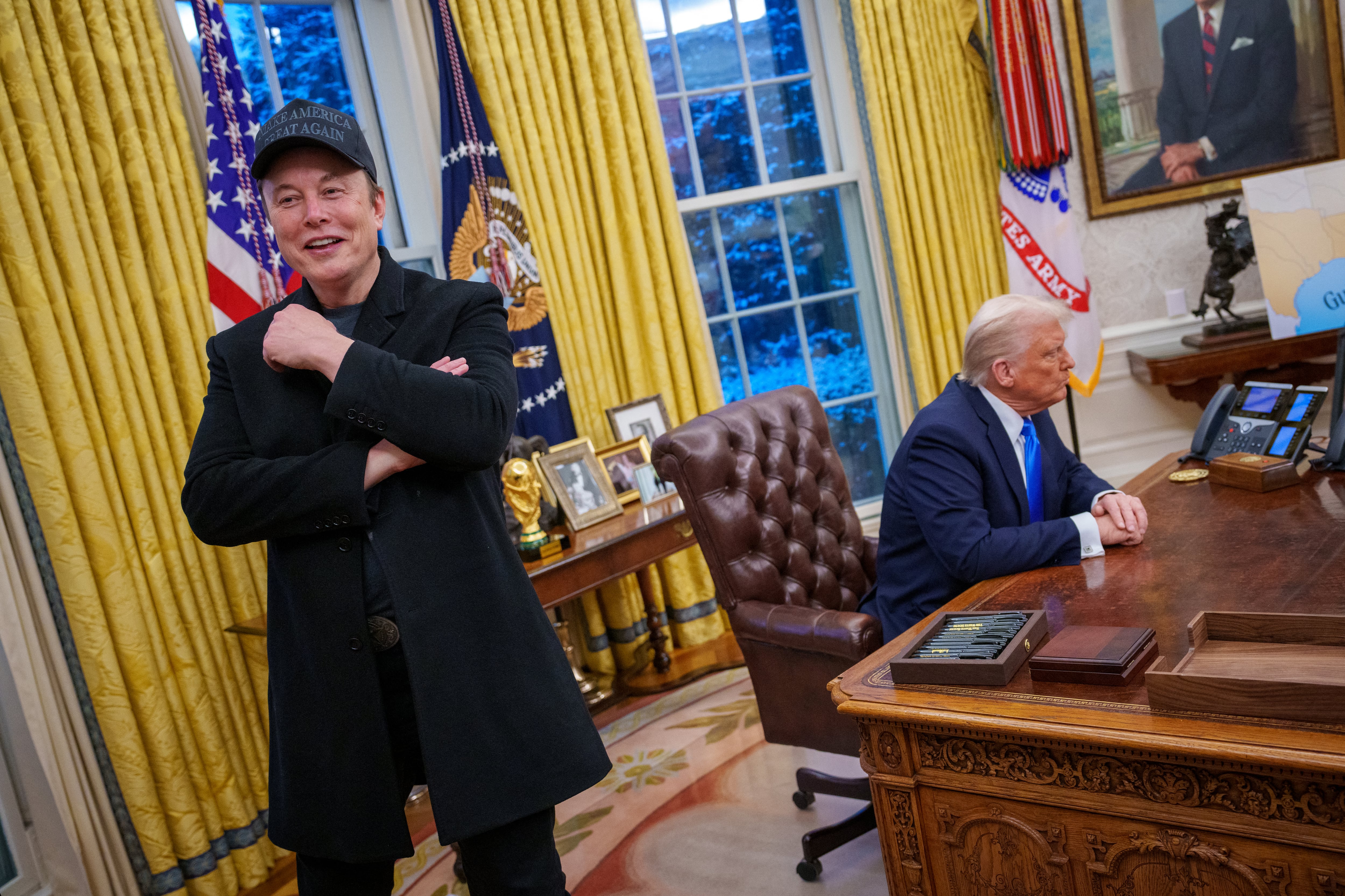 Donald Trump, sentado en el escritorio de la Oficina Oval, y Elon Musk, de pie con una gorra "Make America Great Again", durante una reunión en la Casa Blanca.