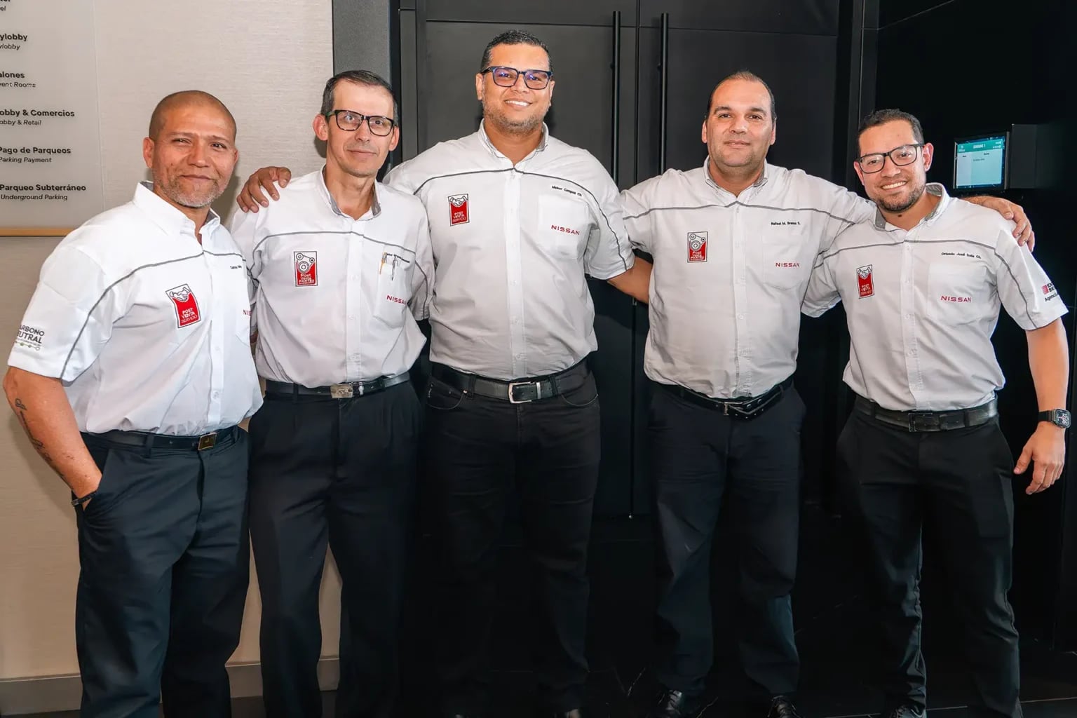 Grupo de cinco personas, empleados, posando juntos con camisas blancas que llevan el logotipo de la marca de automóviles Nissan.