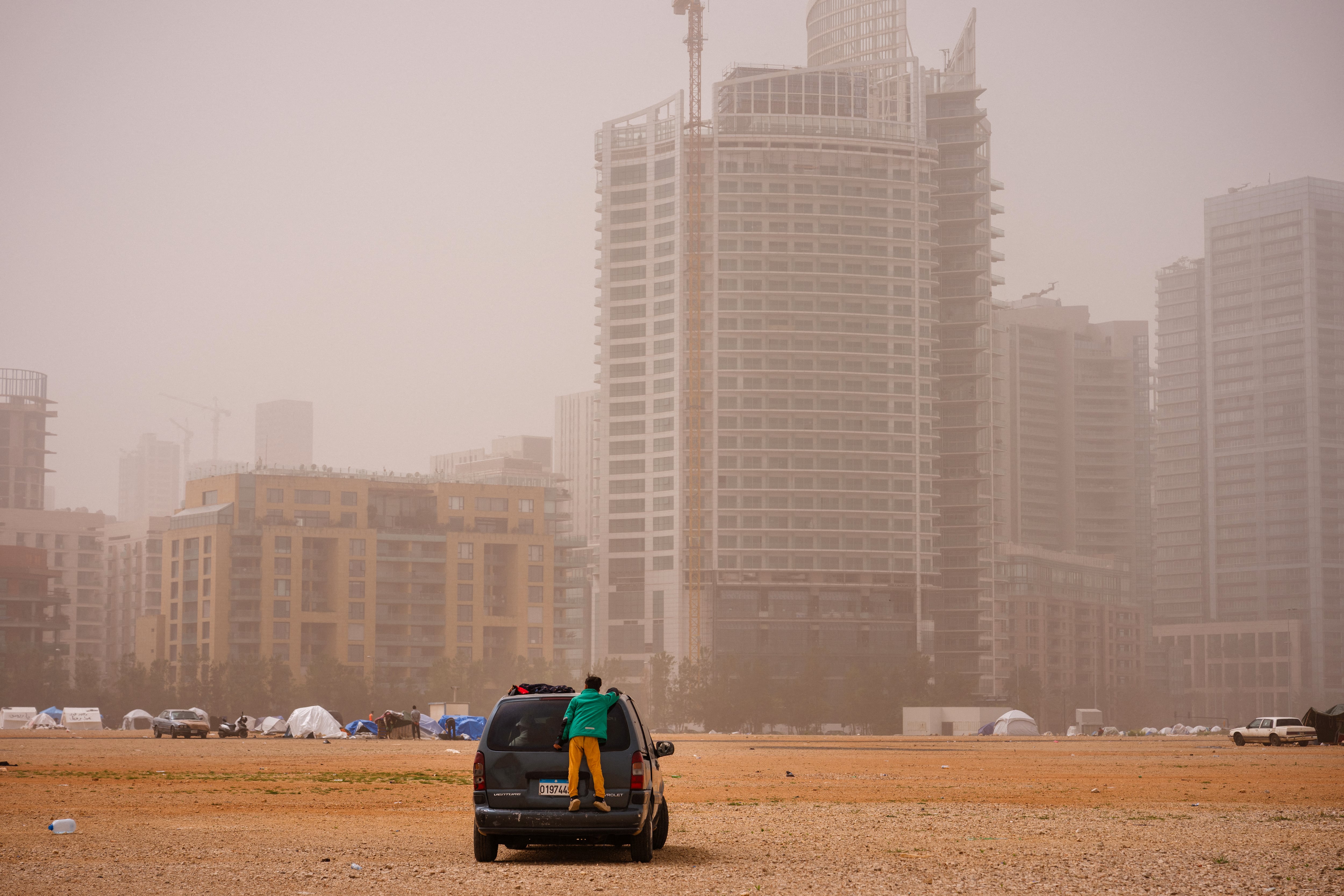 Un niño desplazado se encuentra de pie sobre la parte trasera de un automóvil en un campamento no oficial erigido en la zona costera de Beirut durante una tormenta de arena el 3 de abril de 2026.