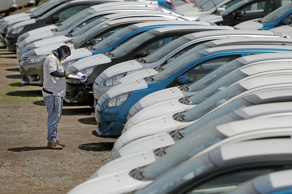 Inspector revisando una fila de automóviles recién importados estacionados en un lote, con impacto en el impuesto a la propiedad de vehículos en Costa Rica por la baja en el tipo de cambio.